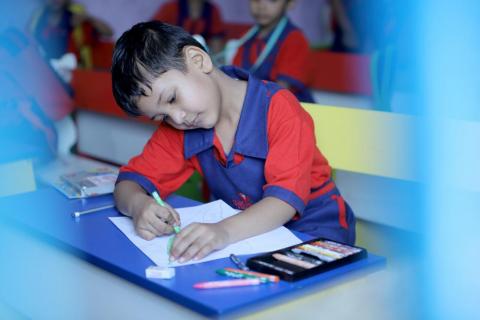 A cute schoolboy is drawing on a white paper