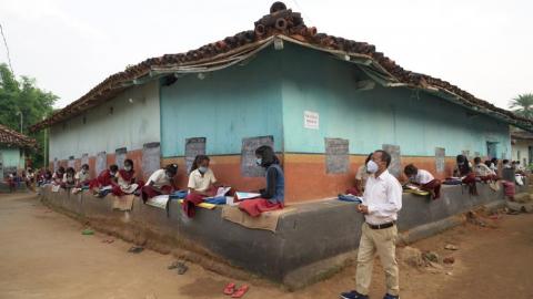 Teacher teaching students outside of the mud house while covid-19